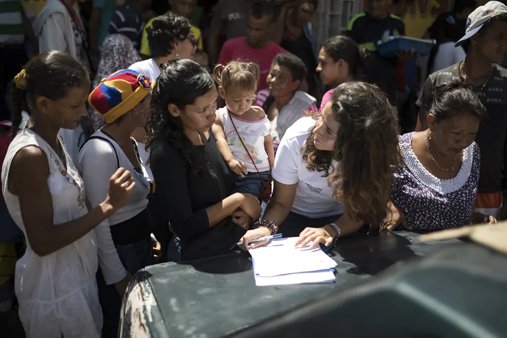 A humanitarian worker assists a mother and her child in registering for aid, amidst a crowd of people seeking assistance.